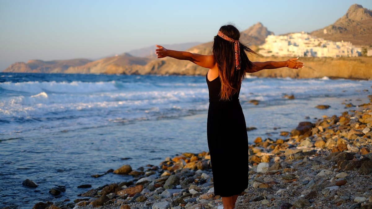 Woman enjoying freedom at sunset on a rocky beach in Greece.